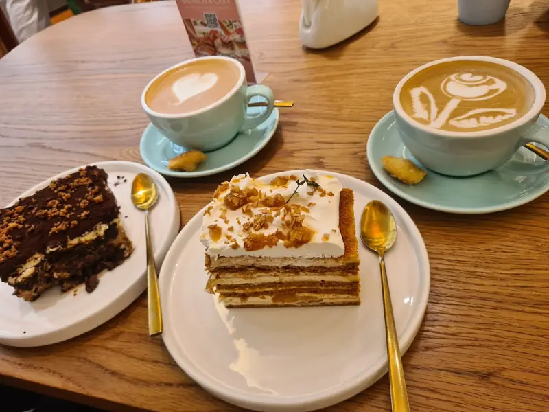 A slice of carrot cake and a chocolate cake with two lattes on a wooden seat at Brunch & Cake Palm Jumeirah