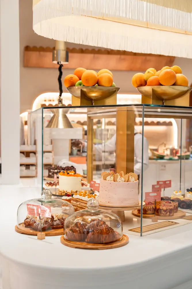 Pastry counter topped with bowls of oranges under a fringed lamp