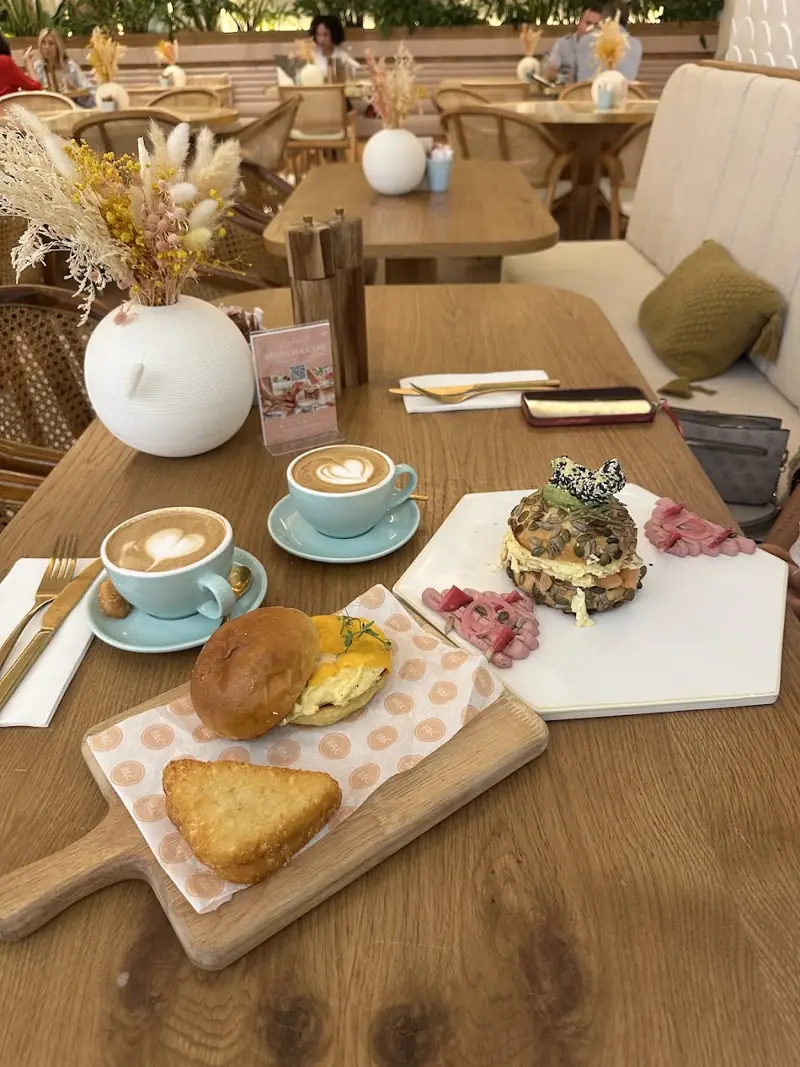 A brunch spread with lattes, croissant toast and a stacked sandwich on a wooden board